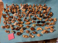 Wide-angle shot showing a large assortment of about 110 Wade enamelled figurines arranged on a blue cloth. The figures include animals (dogs, turtles, butterflies, bears, birds), human forms, and various objects.