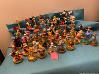Photo of 50 colorful vintage McDonald's Walt Disney figurines arranged on blue cloth showing variety of characters and bases with branding.