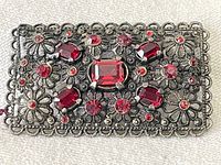 Close-up image of the rectangular silver brooch with 25 red stones illustrating intricate filigree metalwork and varied shapes of red stones, highlighting vintage design.