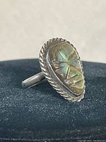 Front view of sterling silver ring with carved abalone shell shaped teardrop with human face design and twisted rope border