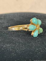 View of the front and side of the gold plated sterling silver ring highlighting the turquoise stones forming a flower shape and the thin band with heart detail.