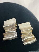 Pair of sterling silver Aurielle earrings shown on black background, displaying their abstract folded metal design.