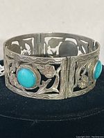 Front angle view showing two turquoise stones and floral cutout design on the silver cuff bracelet.