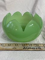 Green jadeite bowl with a petal-shaped rim shown with a measuring ruler indicating size and showing smooth glossy finish.
