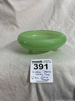 Full side profile of the round light green jadeite candy dish with rolled edge and three feet.