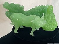 Close-up of green jadeite dragon, water buffalo, and Buddha figurines on black display.