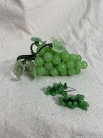 Full view of vintage jadeite grapes sculpture with earrings on fabric background.