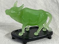 Front-close up of green jadeite water buffalo figurine on black wooden stand, showing the translucent jade color and detailed sculpting.