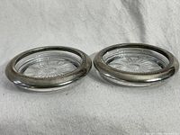 Pair of vintage silver plated round coasters with collar rims and clear daisy patterned glass inserts, side by side on neutral fabric.