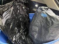 Photo showing three deflated black inflatable air mattresses stored in a blue plastic tub, with visible printed instructions on one mattress.