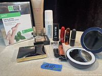 Photo of miscellaneous beauty products including MAC lipsticks, foot treatment mask, compact powders, eyeshadow, mirrors, and skincare sprays.