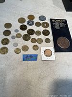 Photo showing the assortment of approximately 28 tokens and coins, including 4 Olympic Coca-Cola tokens and a Moose Factory 1673 token with card.