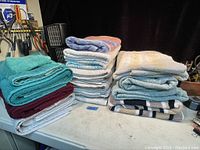 Three stacks of assorted used towels on a table in various colors including teal, maroon, white, blue, and striped.