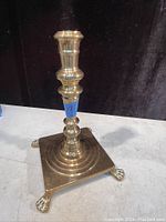 Brass antique candle holder with turned column, square base and claw feet, photographed against black velvet background.
