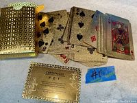 Gold leaf textured playing cards spread out next to the gold certificate plaque and packaging.