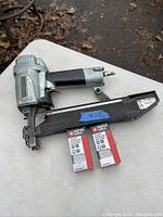 Hitachi pneumatic air staple tool laid on white surface with two boxes of Porter-Cable staples beside it.
