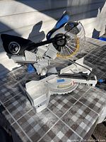 Full view of Kobalt sliding compound miter saw sitting on table outdoors. Visible blade, laser guide, dust collection bag, and controls.