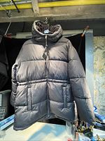 Full view of black ladies winter midi puffer jacket with attached hood displayed on hanger.