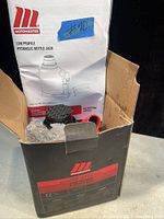Photo of open box showing Motomaster low profile hydraulic bottle jack partially wrapped in bubble wrap with instruction manual inside the box.