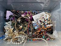 Plastic bin filled with assorted costume jewelry including various bracelets and necklaces of multiple colors and styles.