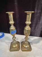 Pair of solid brass antique candle holders with geometric detailing and push rod candle adjustment, standing side by side on a surface.