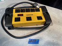 Yellow and black Mastercraft power bar with eight outlets, power switch, and power cord coiled around it on a light gray surface.
