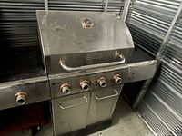Side angle photo showing the stainless steel Elite barbecue with four copper-colored control knobs and stainless steel lid with temperature gauge.