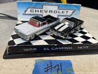 Photo shows two vintage Mattel Chevrolet El Camino die-cast model cars from 1959 and 1970 displayed on a checkered black and white platform with Chevrolet branding.