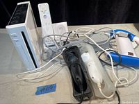 Full lot view showing Nintendo Wii console, two Wii remote controllers with silicone covers, nunchuck controllers, charging dock, and cables.