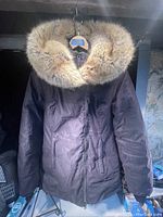 Front view of dark winter down parka with fur-trimmed hood, hanging from hanger.