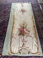 Full view of tapestry panel with central floral bouquet and pale green border on reddish floor