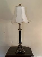 Full view of the antique brass table lamp with fabric shade on a dark wood surface against a beige wall.