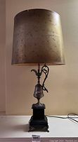 Full view of antique urn lamp with cylindrical gold shade on black base.