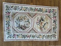 Full view of the antique hooked rug showing both octagonal floral panels and floral border, lying on wooden floor.