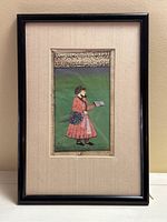 Full view of framed manuscript leaf showing black wood frame, beige mat, painted figure and Arabic text