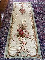 Full view of the tapestry panel laid flat on Persian rug background, showing central floral arrangement and border