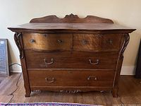 Front view of an antique oak dresser showing four drawers, carved accents on the legs and top backboard, metal handles, and keyholes.