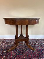 Full front view of the antique round pedestal table showing round top, three carved legs, and brass capped feet.