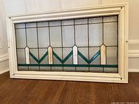 Front view of full stained glass window panel in white-painted frame showing entire geometric design.