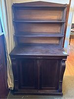 Front view of antique walnut cupboard hutch showing two-door bottom cabinet and three open shelves above with turned spindle supports on the sides. Dark finish with some wear.