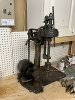 Full side view of drill press showing large worktable, spindle, motor, and mechanical components on wooden workbench.