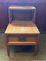 Front angled view showing the two-tier design, single drawer with an X-shaped handle, tapered legs, and surface wear on the lower tier.