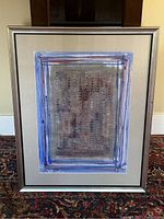 Full front view of the framed abstract watercolor painting showing blue and brown bordered layers around a textured center with small colored marks.