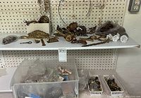 Wide view of assorted vintage brass and ormolu furniture hardware on shelf including drawer pulls, decorative mounts, and other pieces.