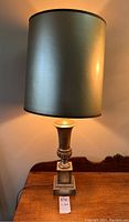 Full view of the vintage table lamp lit, showing silver fabric cylindrical shade and decorative base.