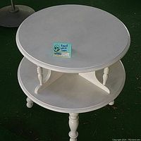 Full view of 22" round white wooden display table featuring the top and lower shelf with turned legs.
