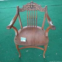 Front view of wooden chair showing carved face detail at backrest and claw armrests with wooden seat