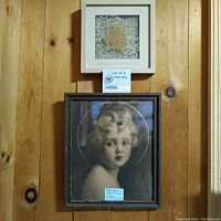 Two wood framed wall art pieces hung on wood-paneled wall: Light of the World Christ Child portrait lower larger piece, Spirit of Hope leaf motif smaller piece above.