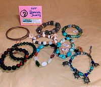 Nine bracelets with various bead colors, styles, and turtle charms arranged on a tan cloth.
