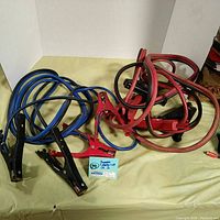 Both sets of jumper cables laid out on a flat yellow surface: one red, one blue, showing cables and clamps coiled and postioned